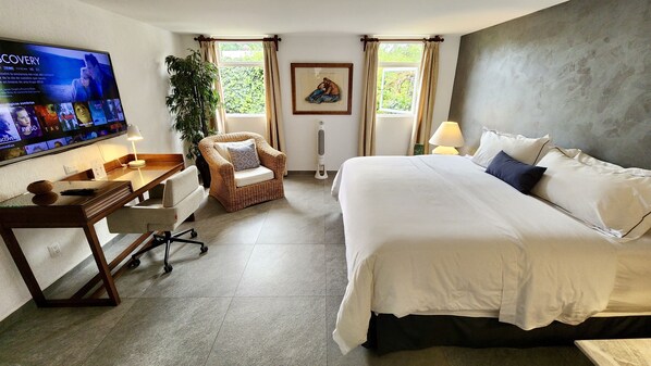 A hotel room with a bed, a desk, a chair, a TV, and a window with curtains. - Casa Tamayo (Mexico City)