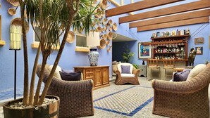 A cozy lounge area with wicker furniture, a bar with various bottles, and decorative baskets on the wall. - Casa Tamayo (Mexico City)