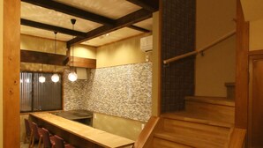 Une cuisine avec un comptoir en bois et des tabourets, un escalier et un mur recouvert de carreaux.