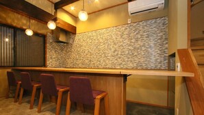 Un espace bar avec des chaises en bois, un mur recouvert de pierres et des luminaires suspendus.