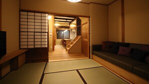 Une pièce de style japonais traditionnel, avec un sol recouvert de tatamis, une basse table en bois, un canapé et une porte coulissante donnant sur un coin cuisine.