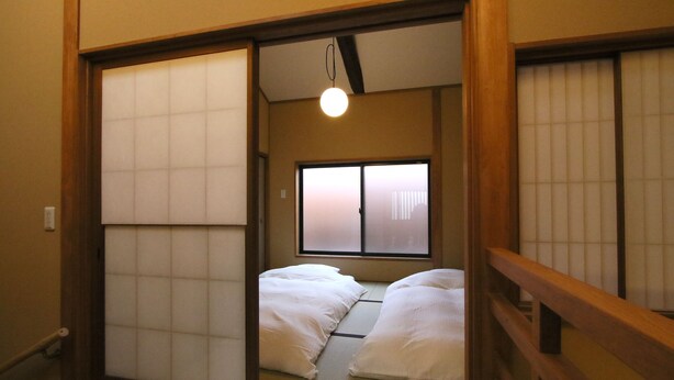 Une pièce de style japonais traditionnel, avec un sol recouvert de tatamis, des portes coulissantes et un lit avec une literie blanche.