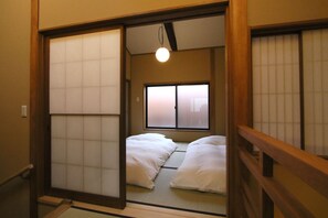 Ein traditioneller japanischer Raum mit Tatami-Böden, Schiebetüren und einem Bett mit weißer Bettwäsche.
