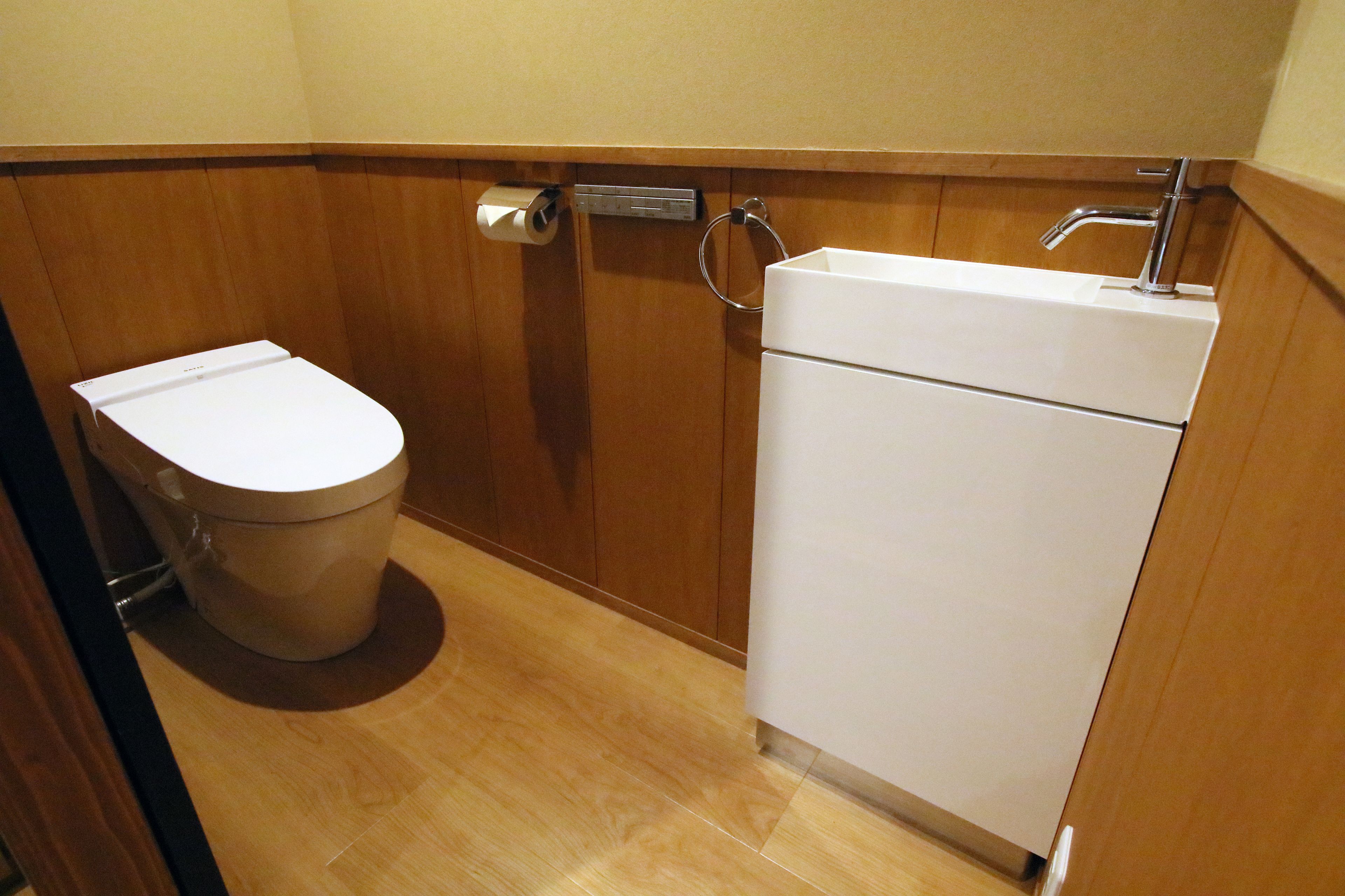 A small, compact bathroom with a toilet, a sink, and a toilet paper dispenser.
