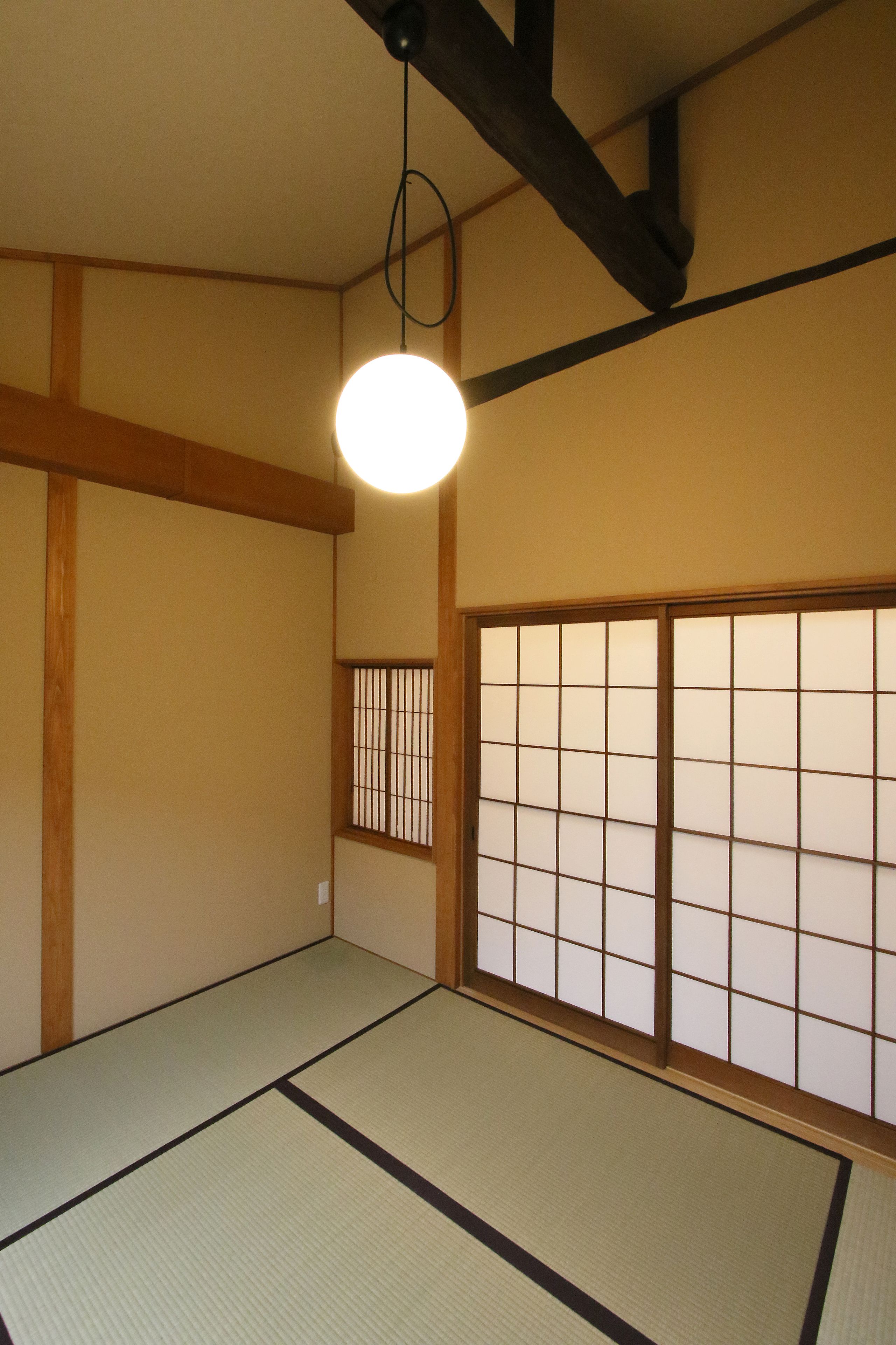Ein traditioneller japanischer Raum mit Tatami-Boden, schiebbaren Shoji-Türen und einer hängenden Leuchte.