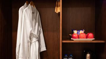 A wooden wardrobe with a robe hanging on a wooden hanger. Inside the wardrobe, there are three red apples on a plate, a bottle of water, and a bag of chips.