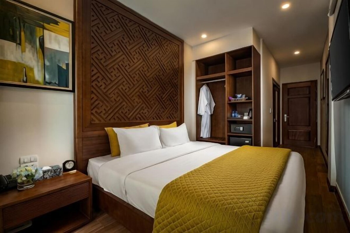 A hotel room with a bed, a nightstand, a wardrobe, and a painting on the wall.