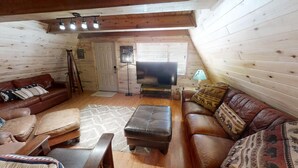 Ein gemütliches Blockhaus-Interieur mit einem braunen Ledersofa, einem passenden Hocker und einem Fernseher in der Ecke.