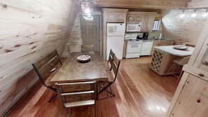 Cozy dining area with a wooden table and metal chairs, adjacent to a kitchenette with a refrigerator, microwave, and stove.