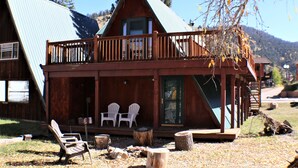 Eine Holzhütte mit Balkon, zwei Adirondack-Stühlen und einem Holztisch.