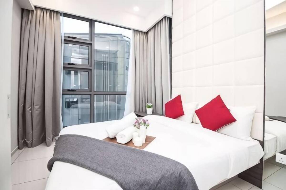A modern hotel room with a large bed, a bedside table with a vase, and a window with curtains.