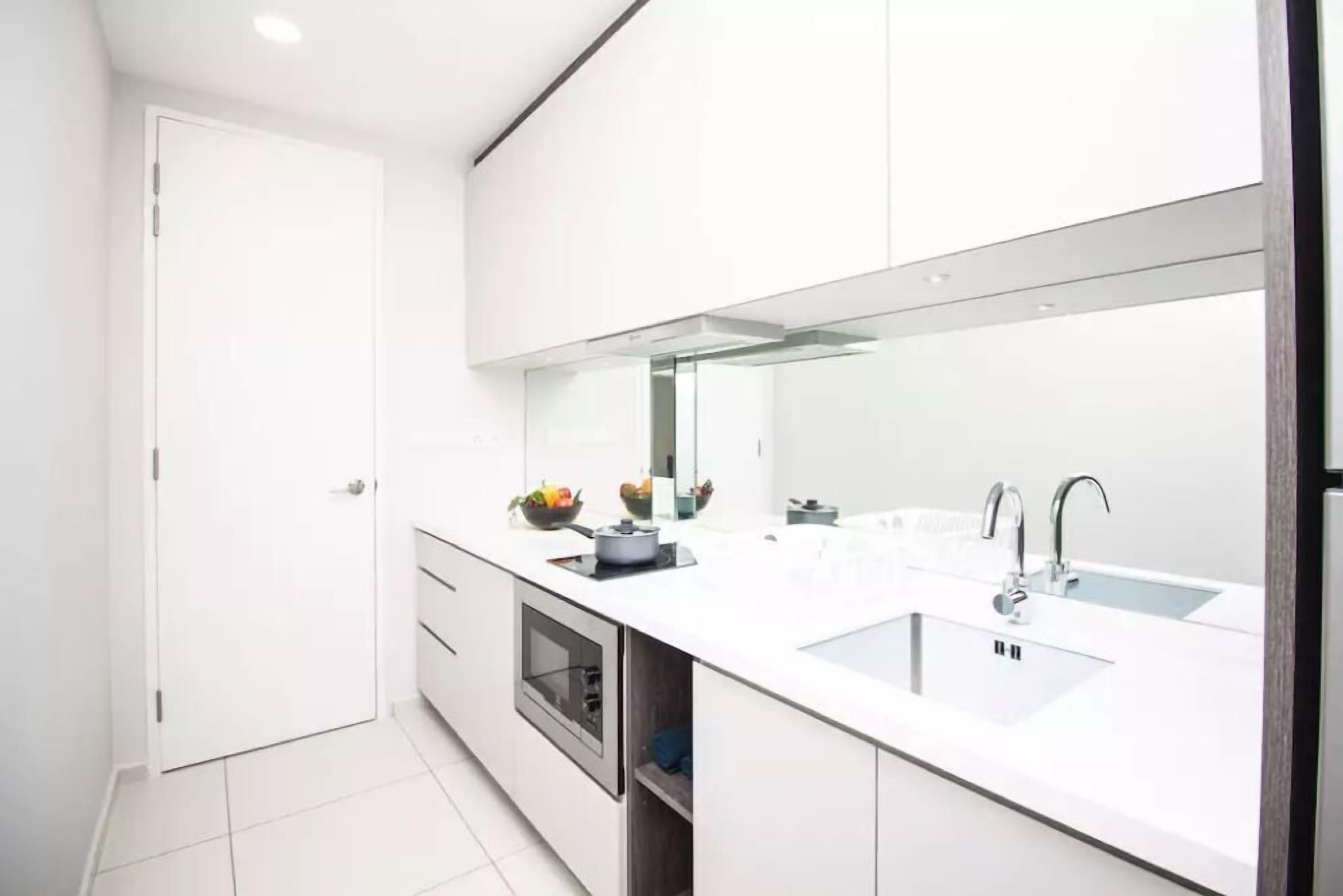 A modern kitchen with white cabinets, a large mirror, a double sink, and a built-in oven.
