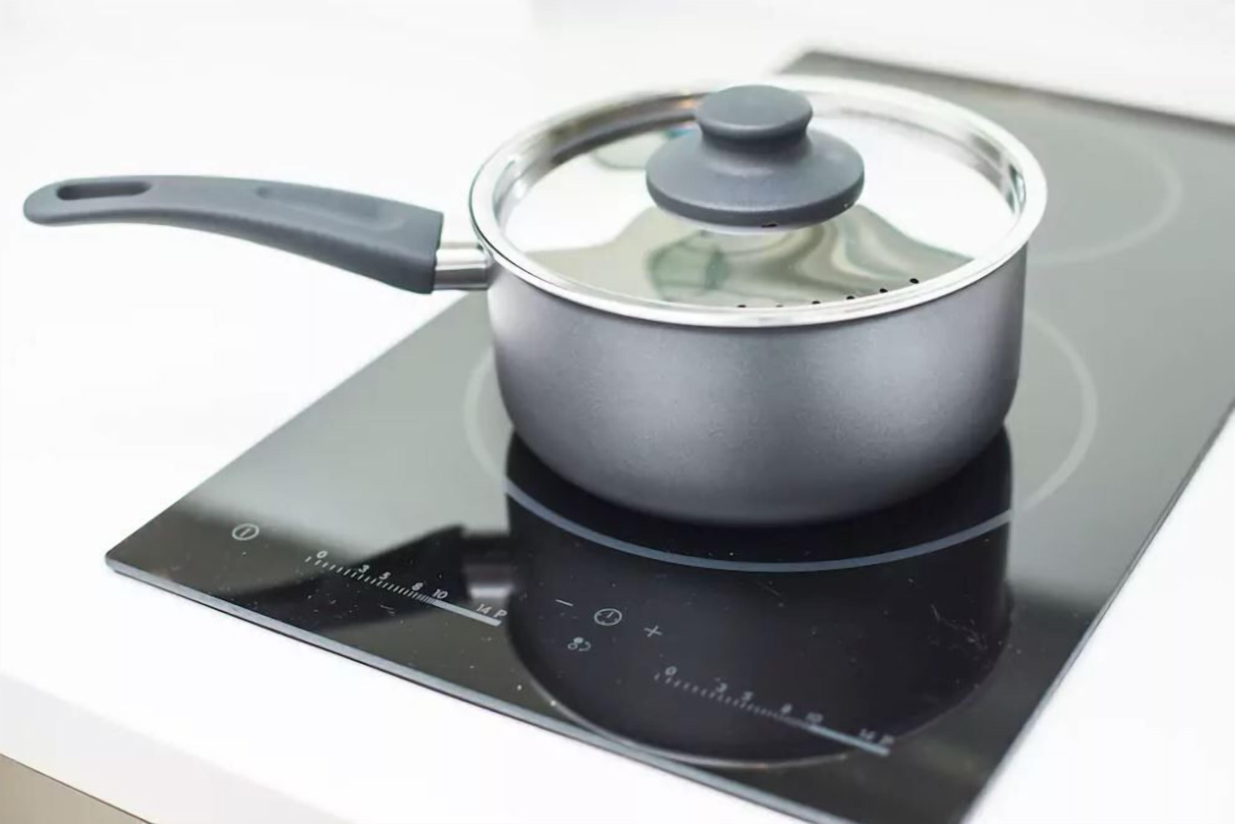 Une plaque de cuisson à induction noire avec une casserole dessus.