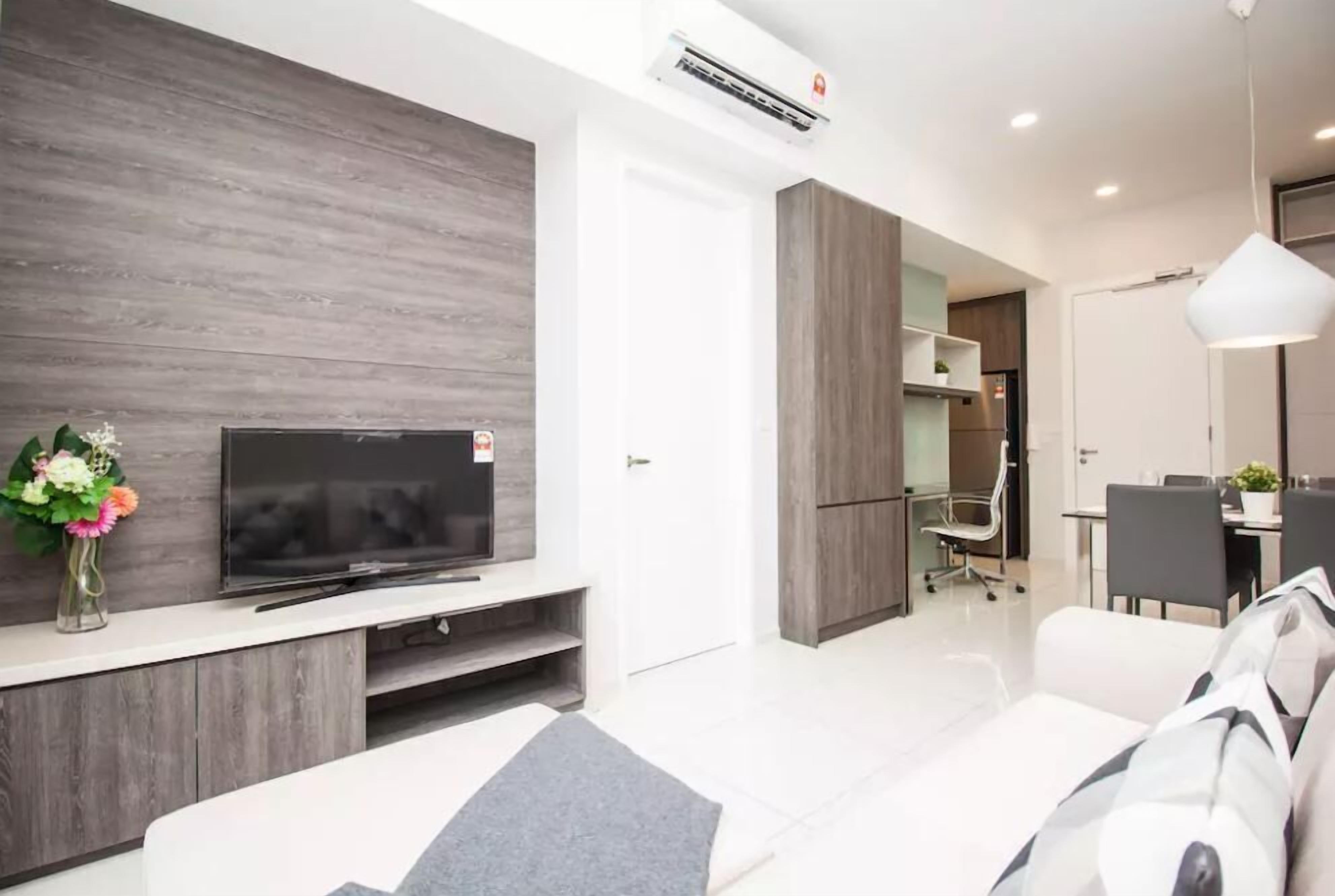 Uma sala de estar moderna com uma TV de tela plana, um sofá e um espaço de jantar com mesa e cadeiras.