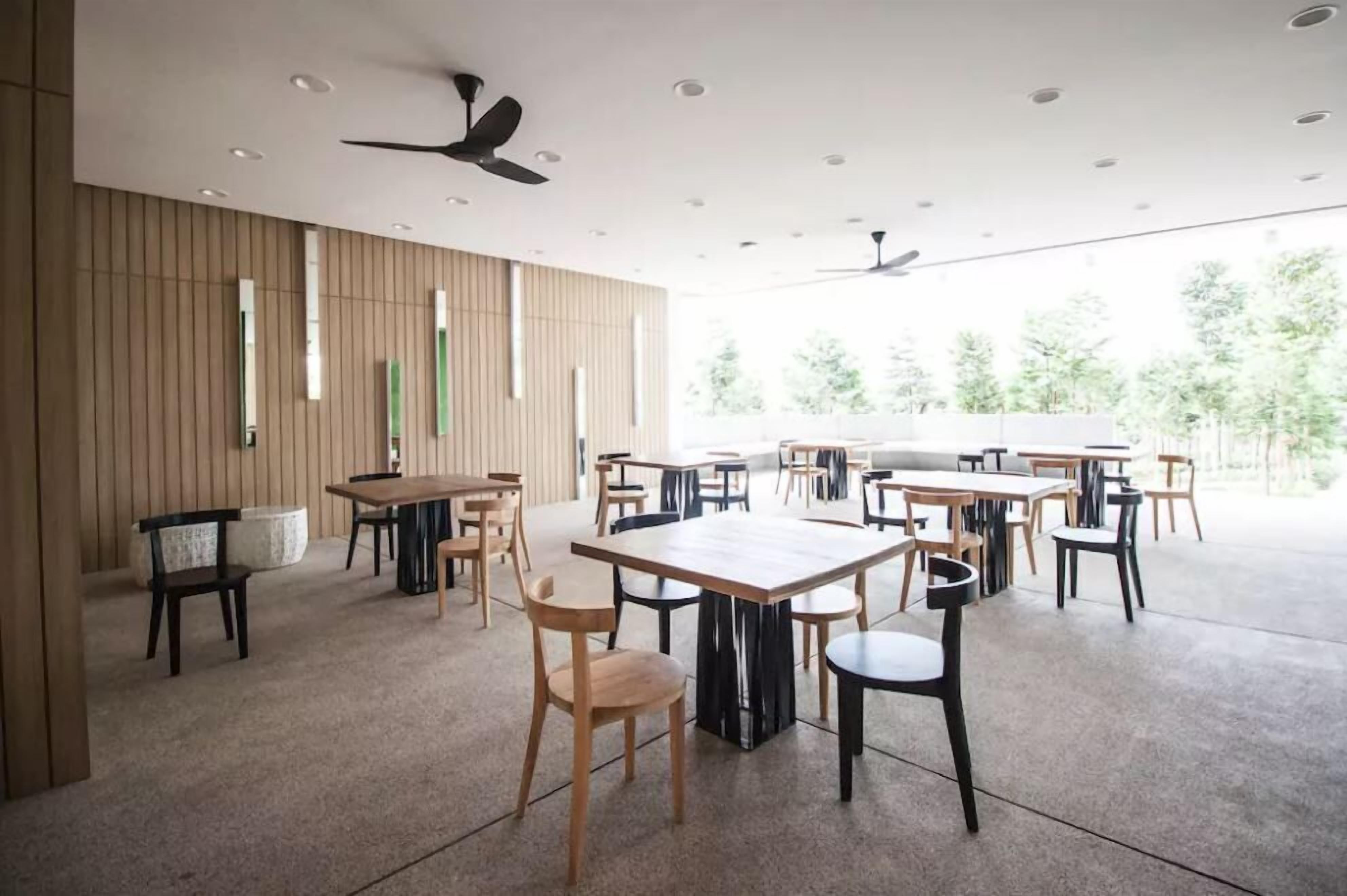 A spacious indoor area with multiple tables and chairs, ceiling fans, and large windows allowing natural light.