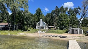 A lakeside cabin with a dock extending into clear water, surrounded by trees and a small shed.