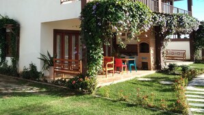 Una casa a due piani con un balcone, un giardino con una panchina di legno e un muro in mattoni.