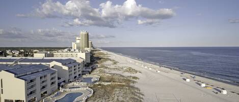 A beachfront hotel with a pool, beach access, and a tall building in the background.