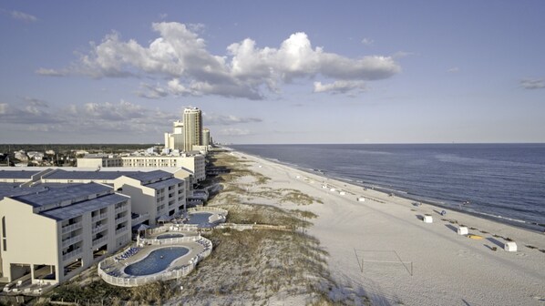 A beachfront hotel with a pool, beach access, and a tall building in the background.
