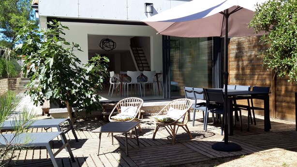 Un patio al aire libre con piso de madera, sillas de mimbre, una mesa y un paraguas grande que da sombra.