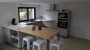 Una cocina moderna con una isla central, taburetes blancos de bar, horno empotrado y ventana con vistas al exterior.