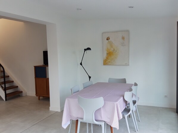 A dining area with a table set for four, white chairs, a black floor lamp, and a painting on the wall.