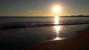 Una playa con el sol reflejándose en el agua y un muelle a lo lejos.