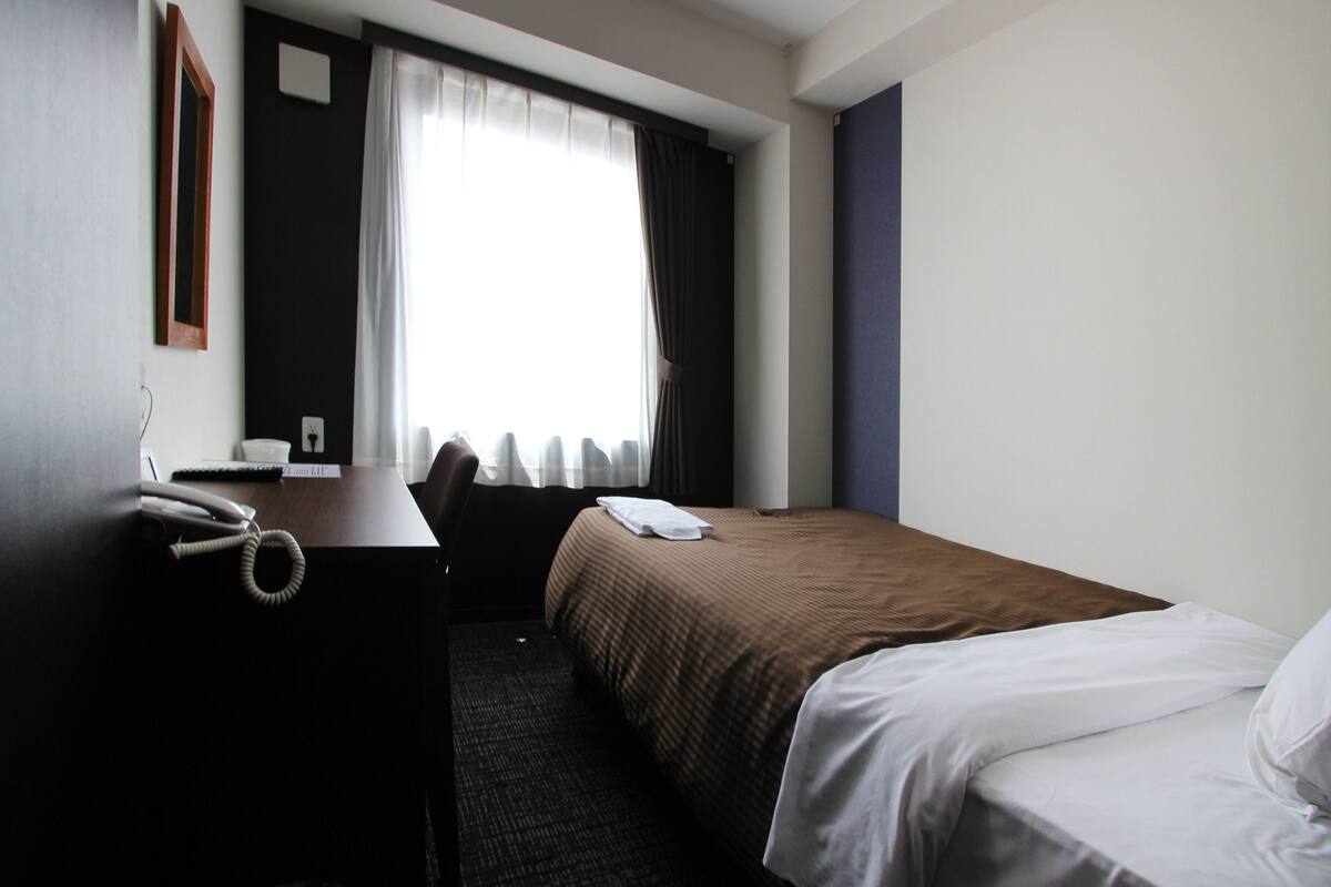 Ein Hotelzimmer mit Bett, Schreibtisch, Telefon und einem Fenster mit Vorhängen.