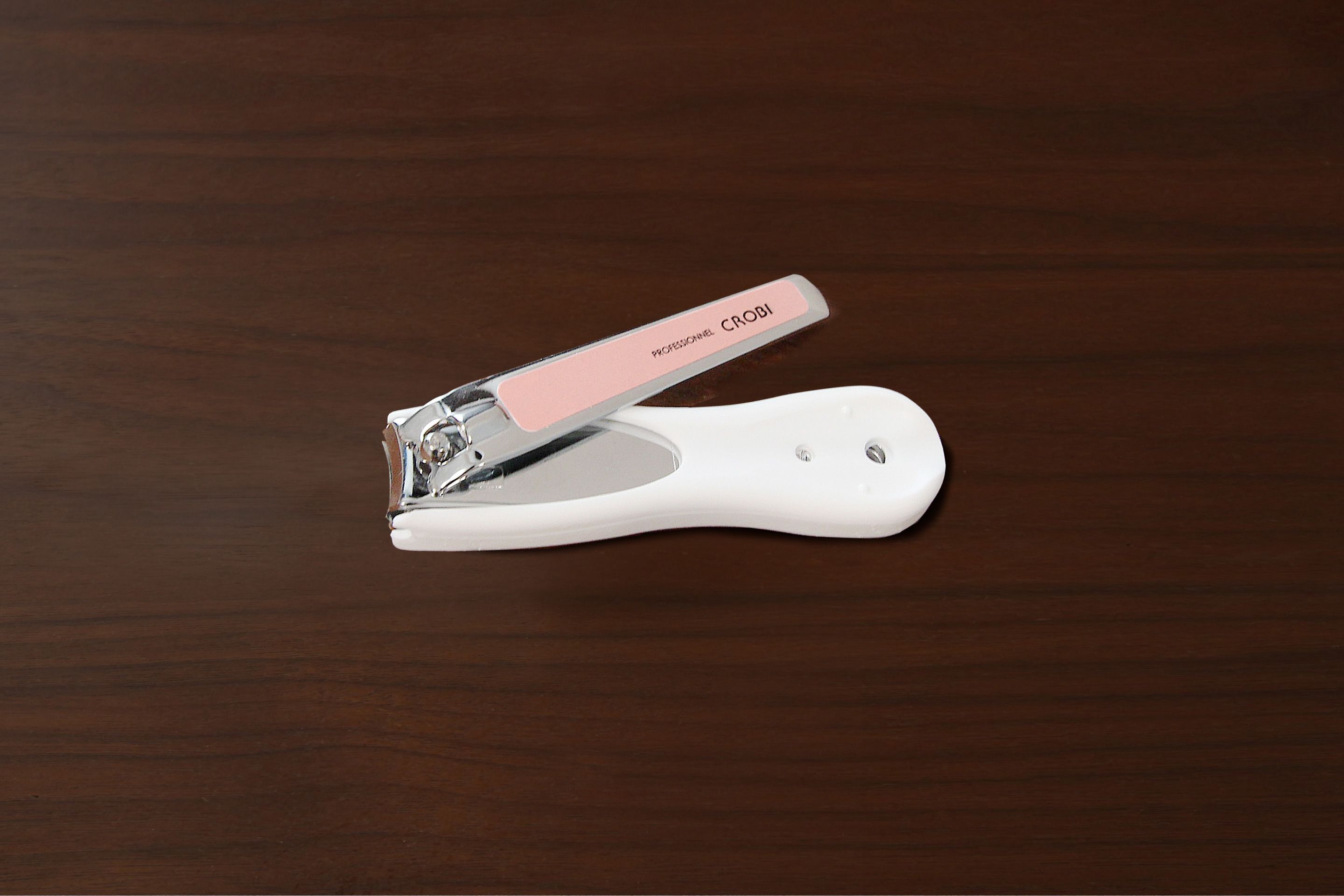 Un cortaúñas blanco con mango rosa sobre una superficie de madera.