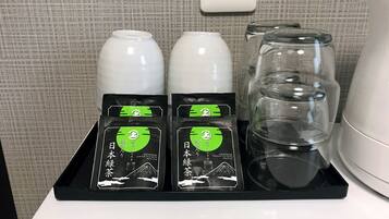 Une assiette contenant quatre sachets de thé vert japonais, deux tasses en céramique blanche et deux verres transparents, le tout posé sur une table.