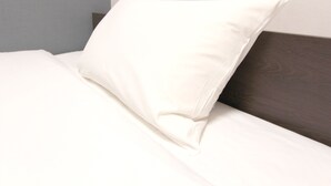 A neatly made bed with a white pillow and a dark wooden headboard. - Hotel Trend Okazaki-Eki Mae (Okazaki)
