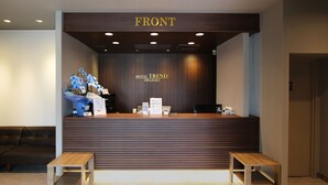 A reception desk with a 'FRONT' sign, a 'HOTEL TREND OKAZAKI' sign, and a reception area with a bench and a sofa. - Hotel Trend Okazaki-Eki Mae (Okazaki)