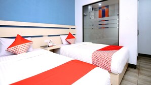 Habitación de hotel con dos camas, cada una con ropa de cama blanca y detalles rojos, un gran ventanal corredero hacia la zona de la ducha y una pared de acento azul.