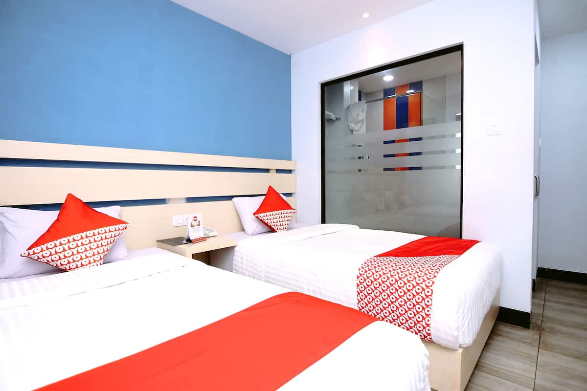 A hotel room with two beds, each with white bedding and red accents, a large sliding glass door to a shower area, and a blue accent wall.