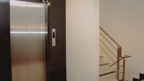 Un ascensor con panel de control y una escalera con barandillas metálicas.