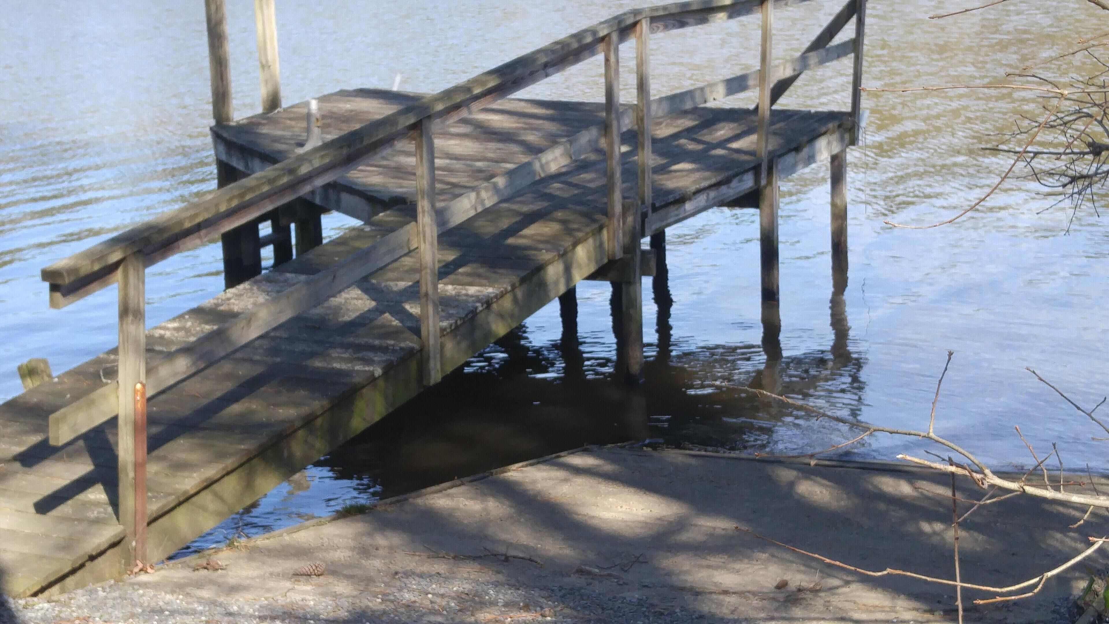 Eine Holzbrücke über Wasser, mit Betonstufen, die hinaufführen.