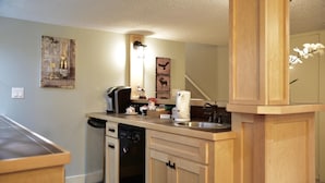 A kitchen with wooden cabinets, a dishwasher, a coffee maker, and wall art including a moose and a bottle. - Calgary Cozy Home (Calgary)