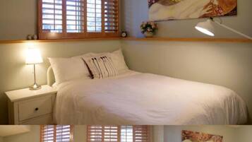 A bedroom with a bed, nightstands, a lamp, a painting, and a window with blinds.