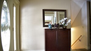 A hallway with a wooden cabinet, a mirror, and a vase with white flowers. - Calgary Cozy Home (Calgary)