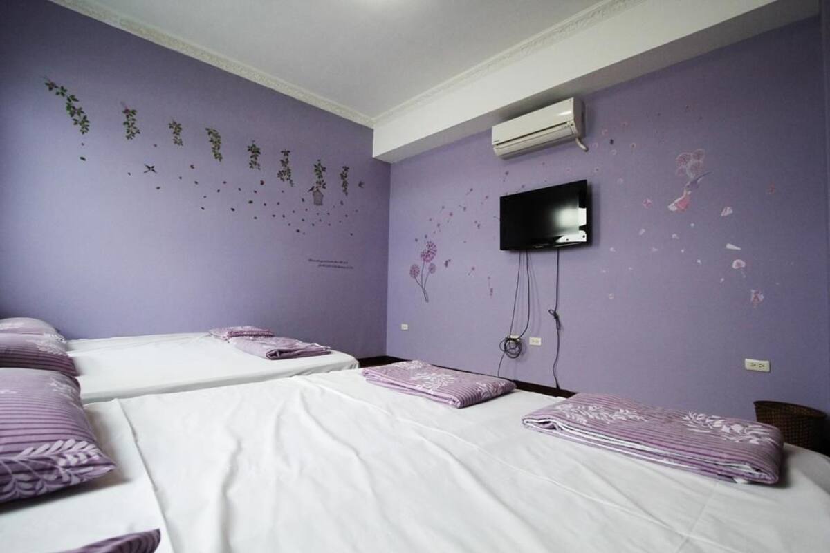 A room with two beds, a flat-screen TV mounted on the wall, and an air conditioning unit.
