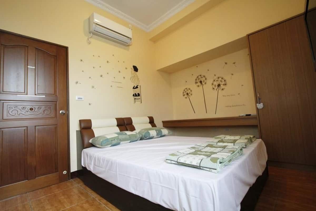 A bedroom with a bed, pillows, a wardrobe, and a wall decoration.