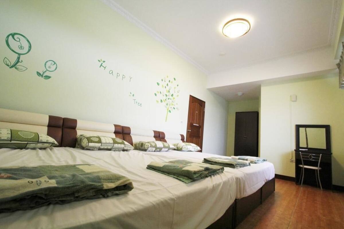A hotel room with two beds, a desk, a chair, a mirror, and a wall with a tree and 'Happy Tree' decoration.