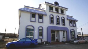 Un edificio de dos pisos con techo plano y una entrada amplia. Hay dos coches estacionados adelante.