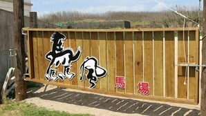 A wooden fence with a black and white animal logo and the text "馬場" (meaning "horse racing" in Chinese).