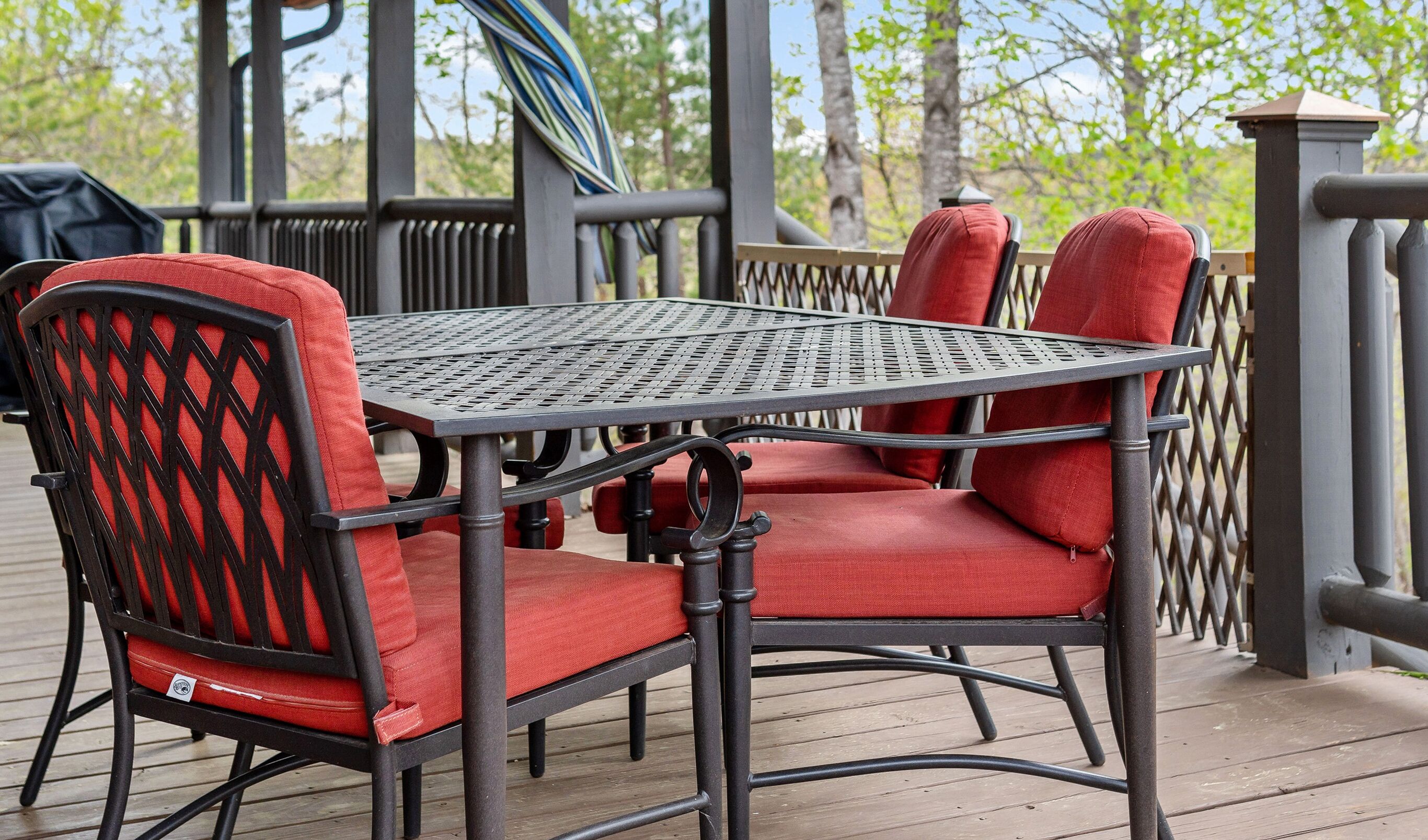 Une table en métal avec des chaises rembourrées de couleur rouge, le tout posé sur une terrasse en bois.