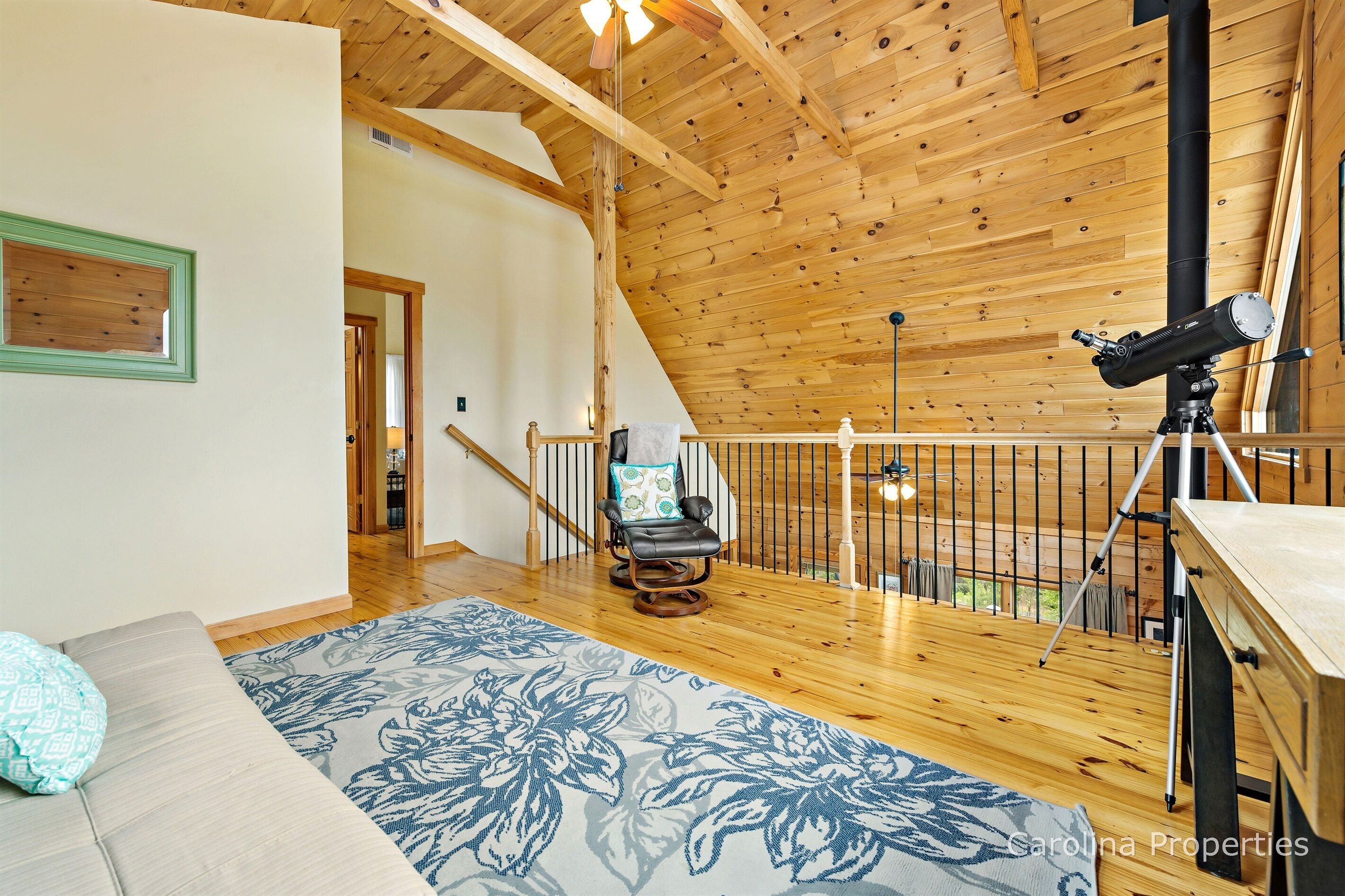 A wooden interior with a telescope on a balcony, a rocking chair, and a patterned rug.