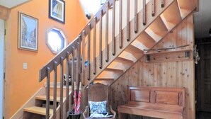 Un escalier en bois avec un banc et une chaise, dans une pièce aux murs orange et dotée d’une fenêtre.
