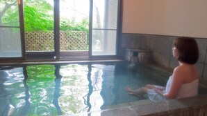 A person sitting in a hot tub with a view of greenery outside. - Kirishima Miyama Hotel (Kirishima)