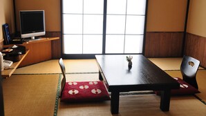 A traditional Japanese room with tatami flooring, a low table, a chair, and a television on a shelf. - Kirishima Miyama Hotel (Kirishima)