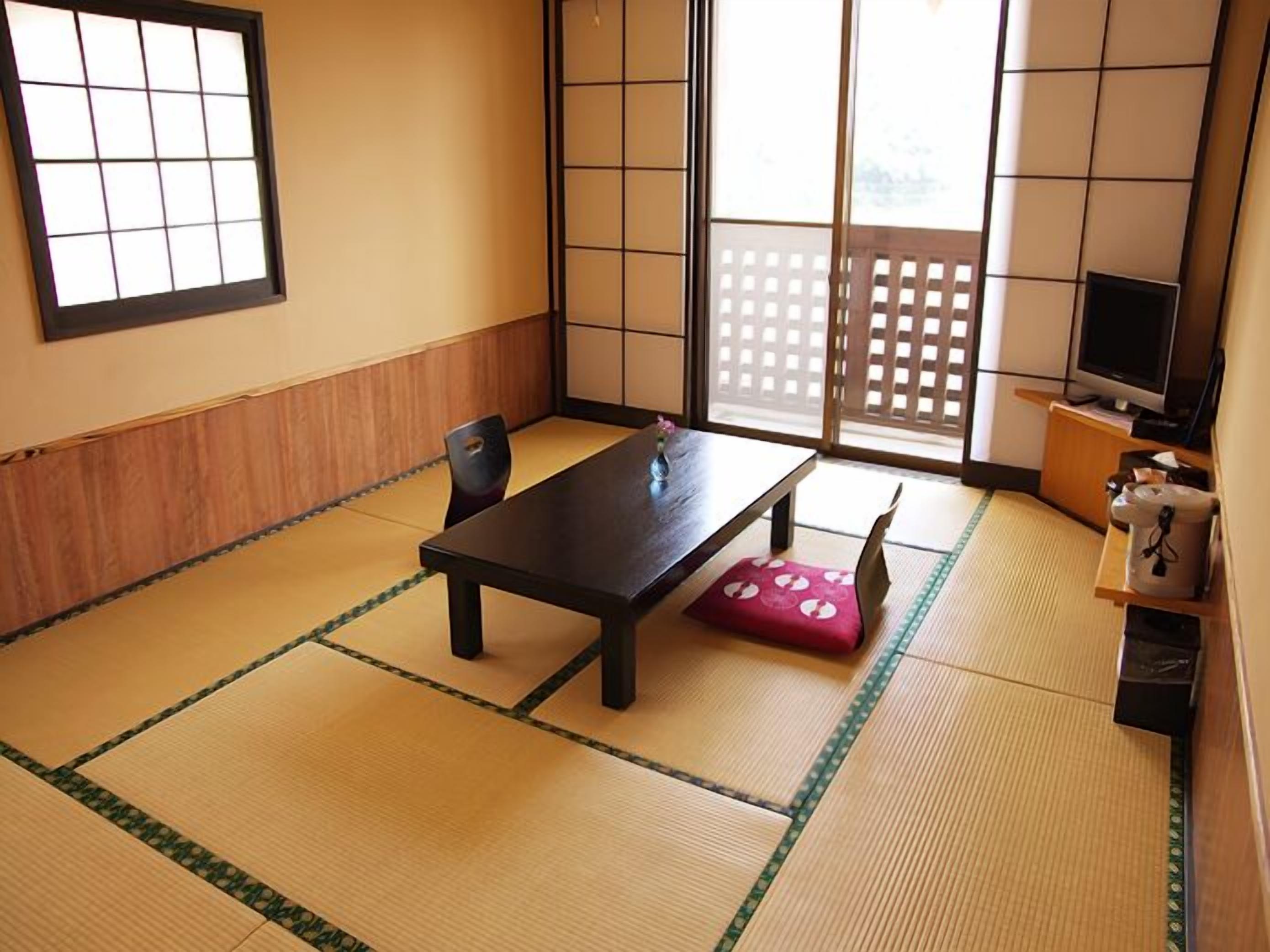 Une pièce traditionnelle avec des tatamis, une petite table, des chaises, un téléviseur et des portes coulissantes.